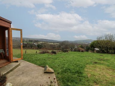 A garden with grass and bushes viewed from a concrete patio with an open wooden door at Ceunant near Newport