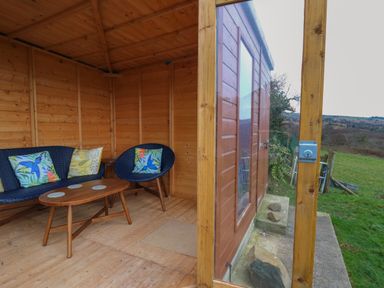 A small wooden room with wicker chairs and a wooden table near a glass wall with an outdoor view at Ceunant near Newport