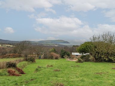 A grassy field with trees and a small building with hills and sea in the background at Ceunant near Newport