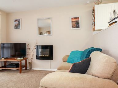 A living room with a beige sofa a television on a wooden stand and framed pictures on the wall at Smugglers Liskeard near St Cleer