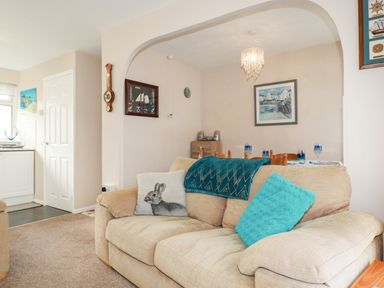 A beige sofa with blue and rabbit cushions in a living room open to a dining area with a table and chairs at Smugglers Liskeard near St Cleer