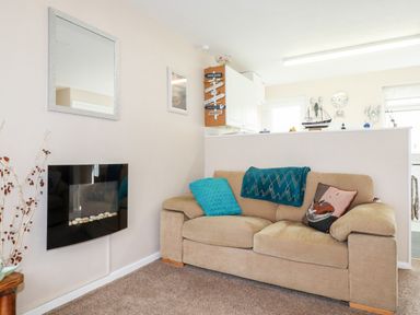 A beige sofa with blue and patterned cushions in a living room with a wall-mounted black fireplace at Smugglers in Liskeard near St Cleer