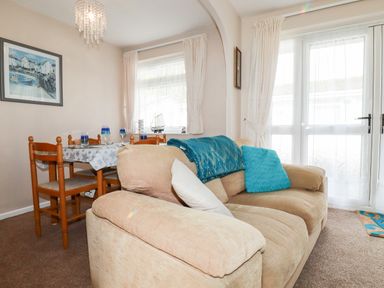 A living room with a beige sofa and blue cushions next to a dining table with wooden chairs at Smugglers in Liskeard near St Cleer