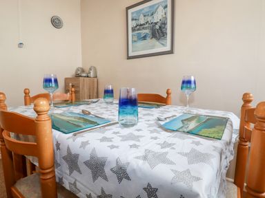 A dining table set with plates glasses and cutlery in a room with wooden chairs a small cabinet and a framed painting at Smugglers in Liskeard near St Cleer