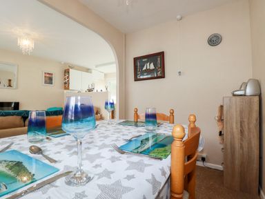 A dining table set with blue gradient glasses and scenic placemats in a room with wooden chairs and a wall decoration at Smugglers in Liskeard near St Cleer