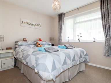 A bedroom with a double bed with gray and white geometric bedding two bedside tables with lamps and a window with curtains at Smugglers in Liskeard near St Cleer