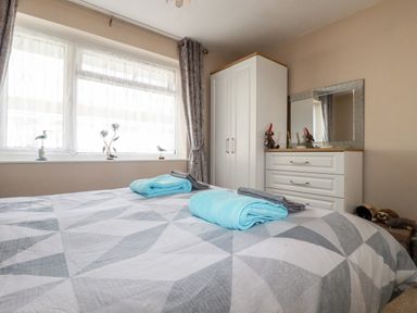 A bedroom with a bed two rolled towels a white wardrobe and a white dresser with a mirror at Smugglers in Liskeard near St Cleer