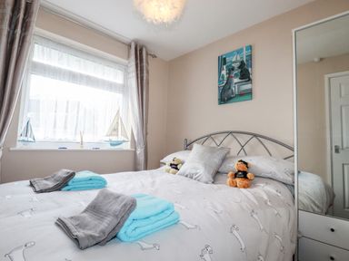 A bedroom with a bed with dog pattern bedding two folded towels on the bed a window with curtains a mirrored wardrobe and wall art of two dogs by The Smugglers in Liskeard near St Cleer