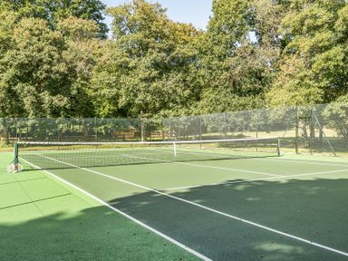 A tennis court with a net and surrounding trees at The Annex in Wimborne Minster
