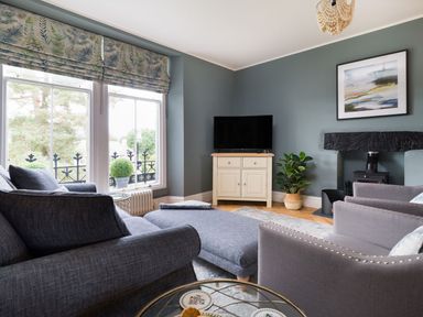 A living room with grey sofas a television on a cabinet and a fireplace at Wansfell at Lipwood House in Windermere