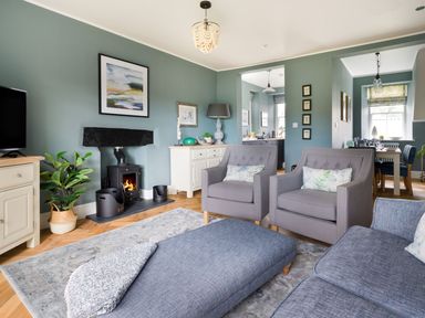 A living room with a wood burning stove two armchairs a sofa and a dining area in the background at Wansfell at Lipwood House in Windermere