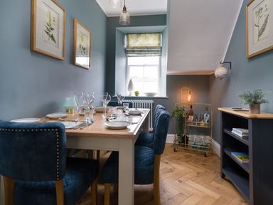 A dining room with a wooden table set with plates and glasses beside a window and a bar cart at Wansfell at Lipwood House in Windermere