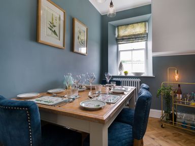 A dining room with a set table with wine glasses and blue upholstered chairs at Wansfell at Lipwood House in Windermere