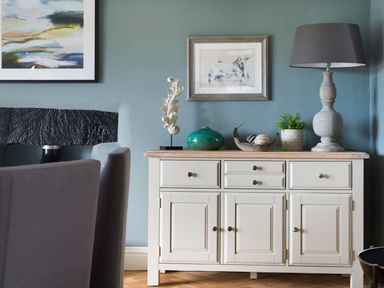 A sideboard with a lamp plant decorative items and framed pictures on the wall at Wansfell at Lipwood House in Windermere