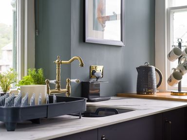 A kitchen sink area with a brass faucet dish rack with utensils a black kettle and mugs on a stand at Wansfell at Lipwood House in Windermere