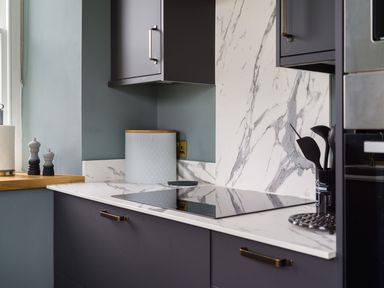 A kitchen countertop with an electric stovetop a marble backsplash and cooking utensils at Wansfell at Lipwood House in Windermere