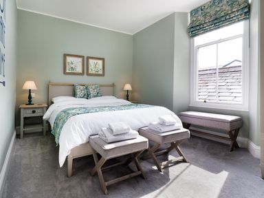 A bedroom with a double bed two bedside tables two stools with towels a bench under a window at Wansfell at Lipwood House in Windermere