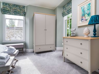 A bedroom with a wardrobe a dresser and two windows with patterned blinds at Wansfell at Lipwood House in Windermere