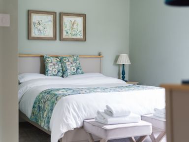 A bedroom with a bed with patterned cushions and runner white bedding and towels on stools a lamp on a bedside table and framed pictures on the wall at Wansfell at Lipwood House in Windermere