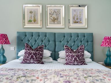 A bedroom with a double bed with teal tufted headboards purple pillows floral bedspread and bedside lamps at Wansfell at Lipwood House in Windermere