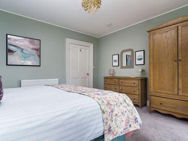 A bedroom with a bed a wooden dresser a wooden wardrobe and framed artwork on the walls at Wansfell at Lipwood House in Windermere