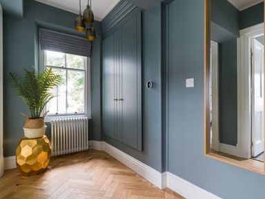 A corner of a room with a window radiator built in cabinet wall mirror and plant on a textured gold stand at Wansfell at Lipwood House in Windermere