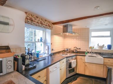 A kitchen with wooden cabinets a gas stove microwave dishwasher and two windows at Naunton Cottage in Lyme Regis