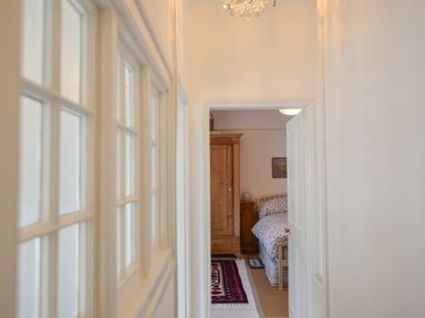 A hallway leading to a bedroom with a wooden wardrobe bed and rugs at Naunton Cottage in Lyme Regis