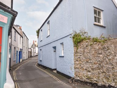 A narrow street with pastel colored houses and a stone wall at Naunton Cottage in Lyme Regis