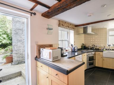 A kitchen with wooden cabinets a microwave stove and sink with a window and door leading outside at Naunton Cottage in Lyme Regis