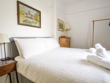 A bedroom with a bed with white linens folded towels bedside tables lamps and paintings on the walls at Naunton Cottage in Lyme Regis