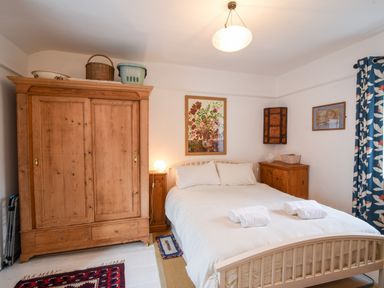 A bedroom with a bed with white linens a wooden wardrobe wooden furniture and floral curtains at Naunton Cottage in Lyme Regis