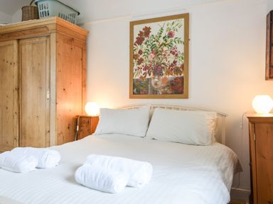 A bedroom with a double bed two bedside tables wooden wardrobe and floral painting at Naunton Cottage Lyme Regis