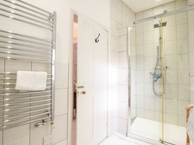 A bathroom with a chrome towel radiator a glass shower enclosure and a white door at Naunton Cottage in Lyme Regis