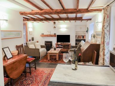 A living room with sofas a coffee table and a television near wooden beams on the ceiling at Naunton Cottage in Lyme Regis
