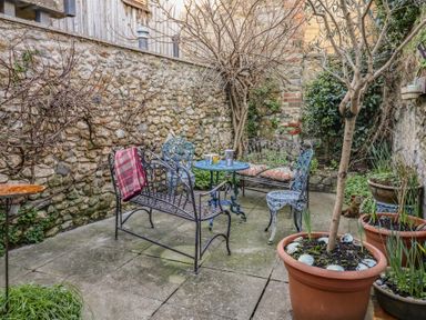 An outdoor patio with metal furniture a table with cups and a coffee pot stone walls and potted plants at Naunton Cottage in Lyme Regis