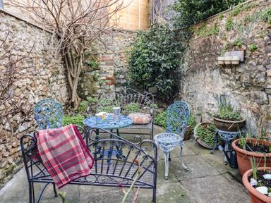A small stone courtyard with iron garden furniture and potted plants at Naunton Cottage Lyme Regis