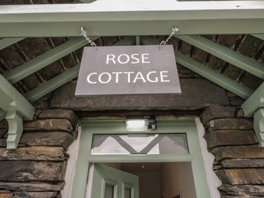 A hanging sign reading Rose Cottage above a green door in a stone wall