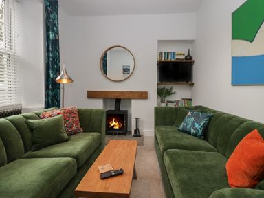 A living room with two green sofas a wooden coffee table a fireplace a round mirror and a TV on shelves at Rose Cottage in Ambleside