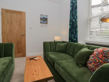 A living room with green sofas a wooden table a lamp a door and window blinds at Rose Cottage in Ambleside