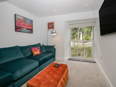 A living room with a green sofa and an orange ottoman by a window at Rose Cottage Ambleside