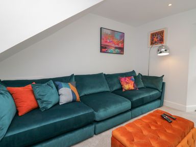A living room with a teal sofa and colorful cushions and an orange ottoman with remote controls at Rose Cottage in Ambleside