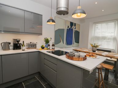 A kitchen with grey cabinets white countertops pendant lights and a dining table with placemats and flowers at Rose Cottage in Ambleside