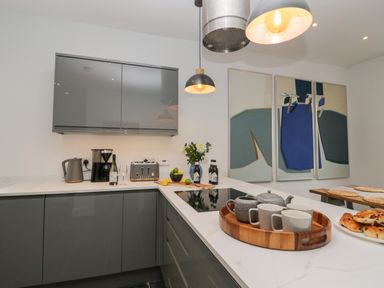 A modern kitchen with grey cabinets a white countertop pendant lights and abstract paintings on the wall at Rose Cottage in Ambleside