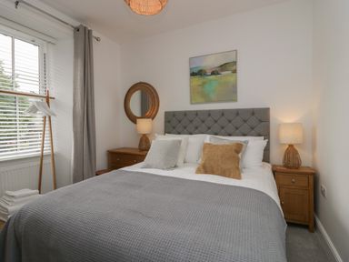 A bedroom with a bed with grey and brown pillows bedside tables with lamps and a window with curtains at Rose Cottage Ambleside