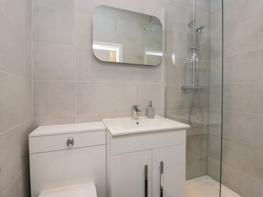 A bathroom with a sink, mirror, shower area, and toilet at Rose Cottage in Ambleside