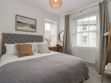 A bedroom with a bed with pillows a desk with a lamp a round mirror windows with blinds and curtains at Rose Cottage in Ambleside