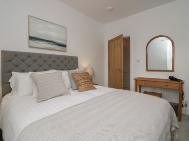A bedroom with a bed with pillows and a blanket a wooden desk with a mirror and a lamp at Rose Cottage in Ambleside