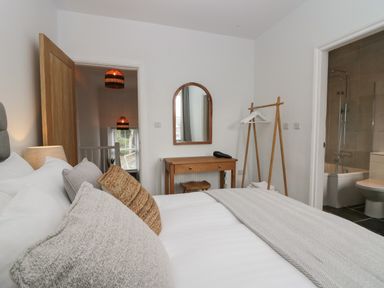 A bedroom with a bed pillows a wooden dressing table a mirror a wooden clothes rack and an open door to a bathroom at Rose Cottage in Ambleside