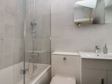A bathroom with a bathtub and shower, a toilet, a sink with a faucet, a soap dispenser, and a wall mirror at Rose Cottage in Ambleside